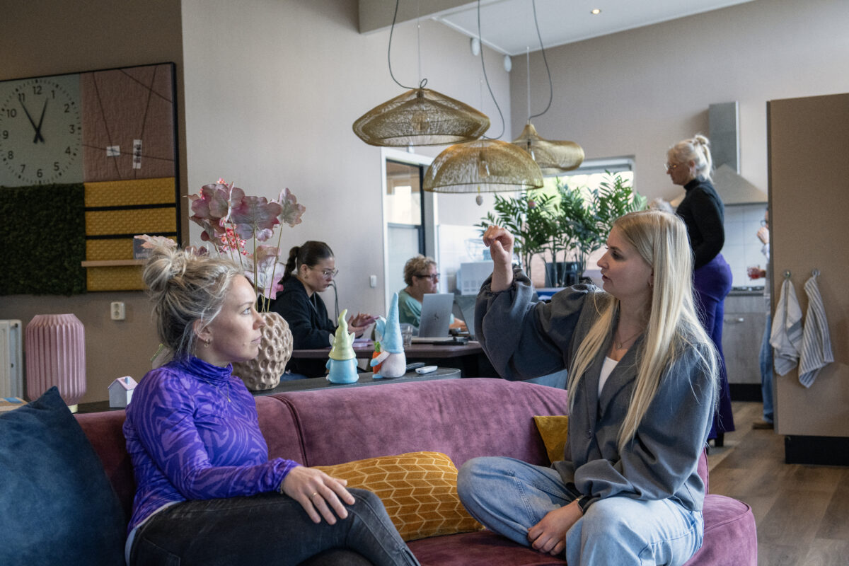 2 medewerkers op de bank in gesprek, andere collega's op de achtergrond
